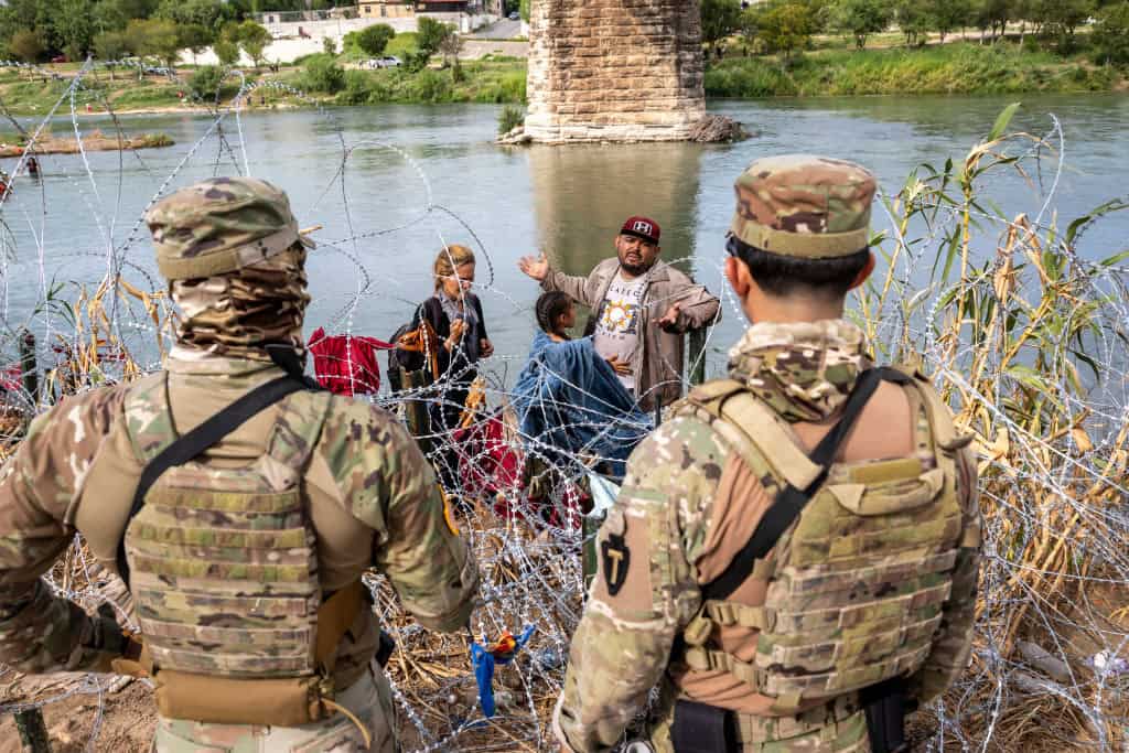 soldiers watch migrants at the border